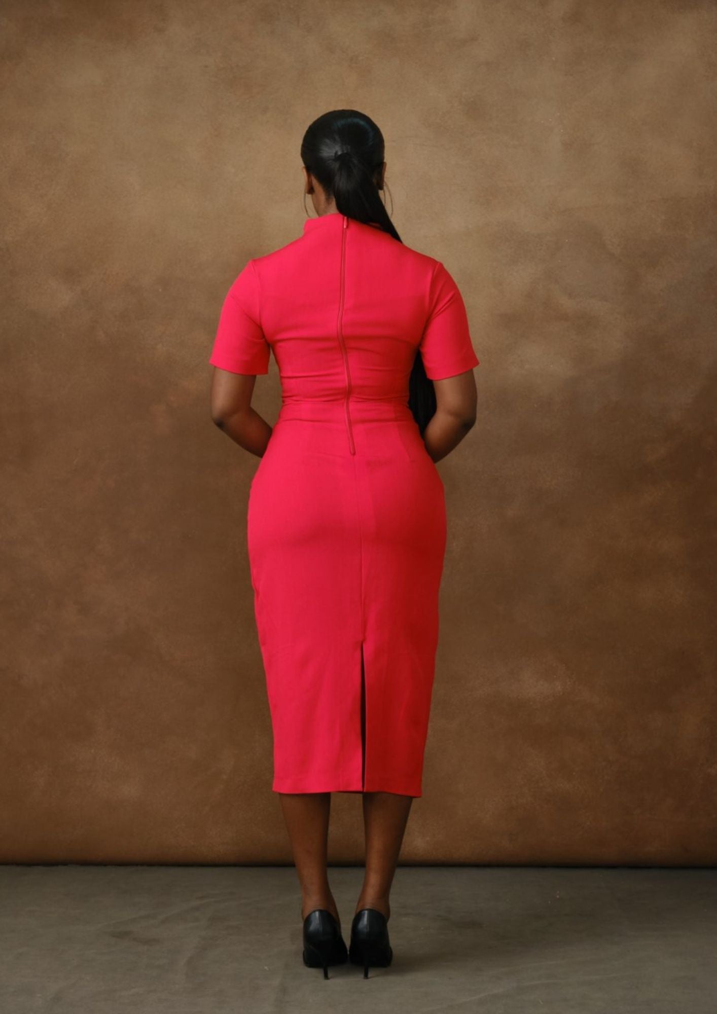 Woman in fitted pink midi dress with short sleeves, back view, seamless brown background