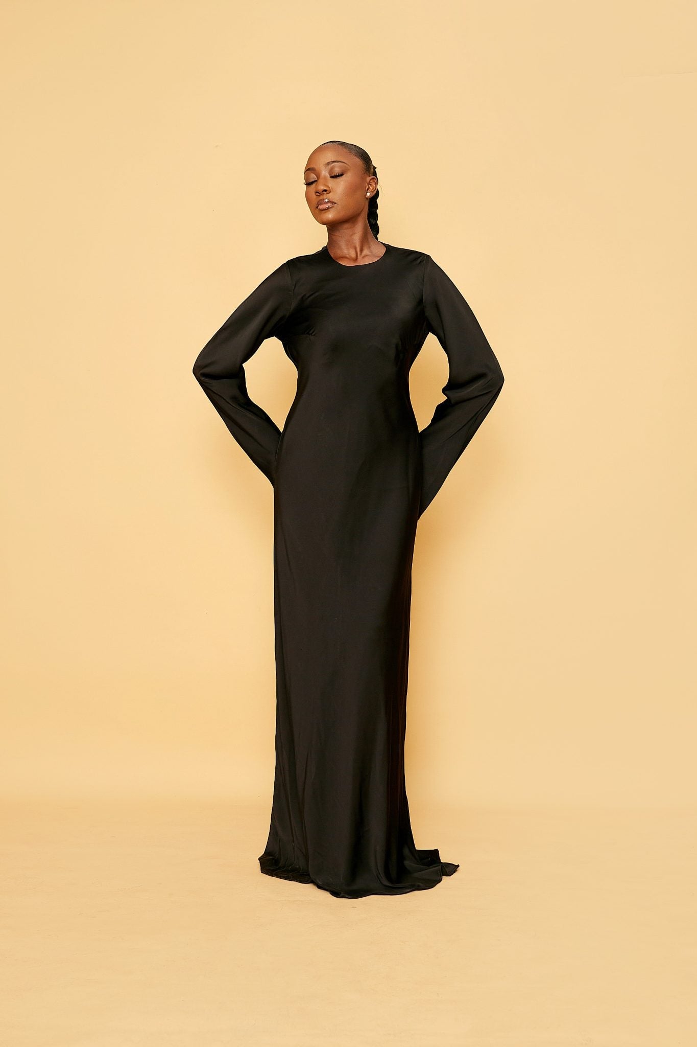 Elegant woman in a long black dress posing against a beige background